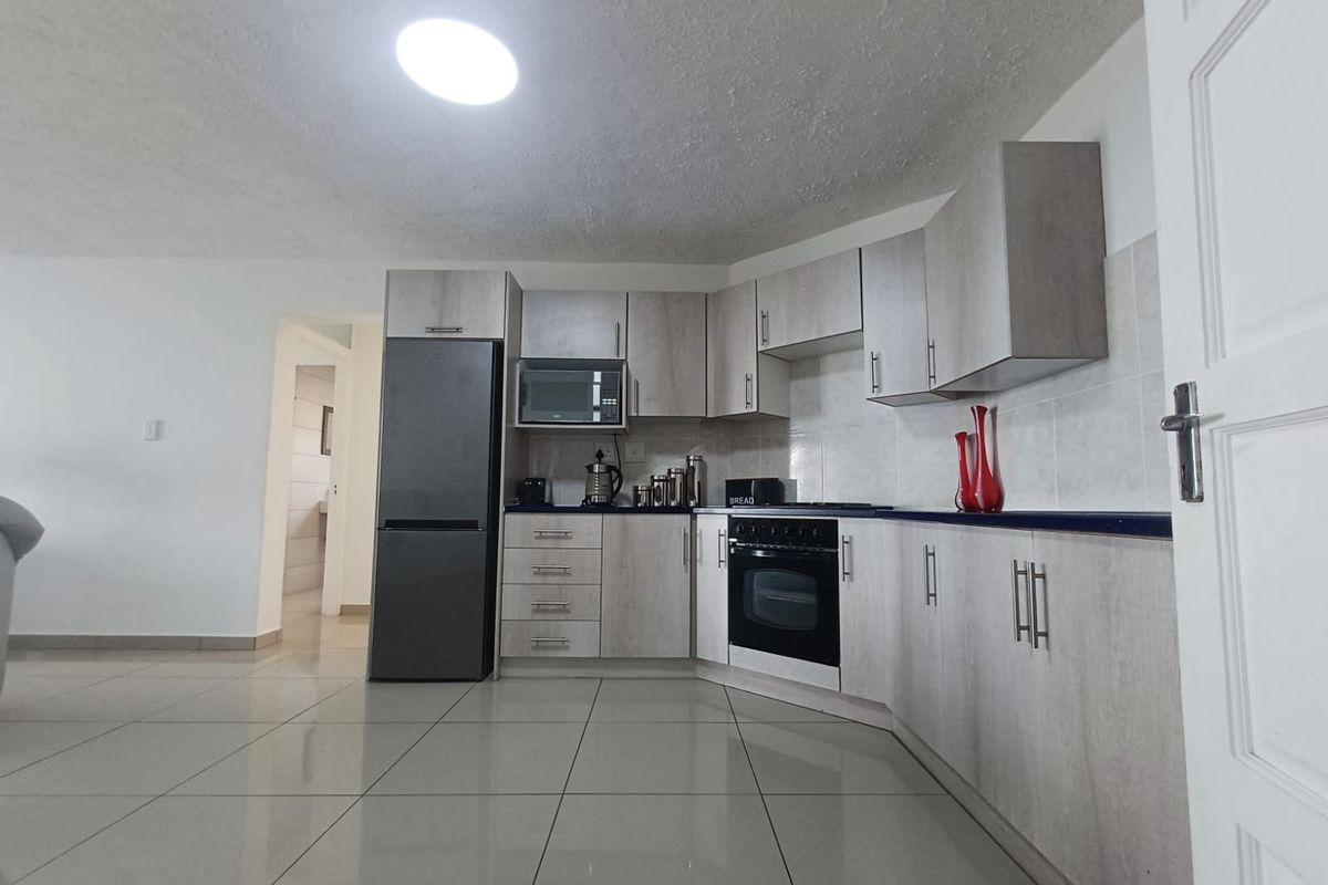 A modern kitchen featuring light wood-grain cabinetry, dark countertops, built-in oven, and microwave, complemented by neutral tiled flooring.