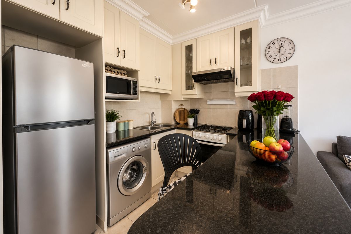 A well-appointed kitchen featuring cream cabinetry, granite countertops, a gas hob, extractor fan, and integrated laundry facilities, offering a functional and modern layout.