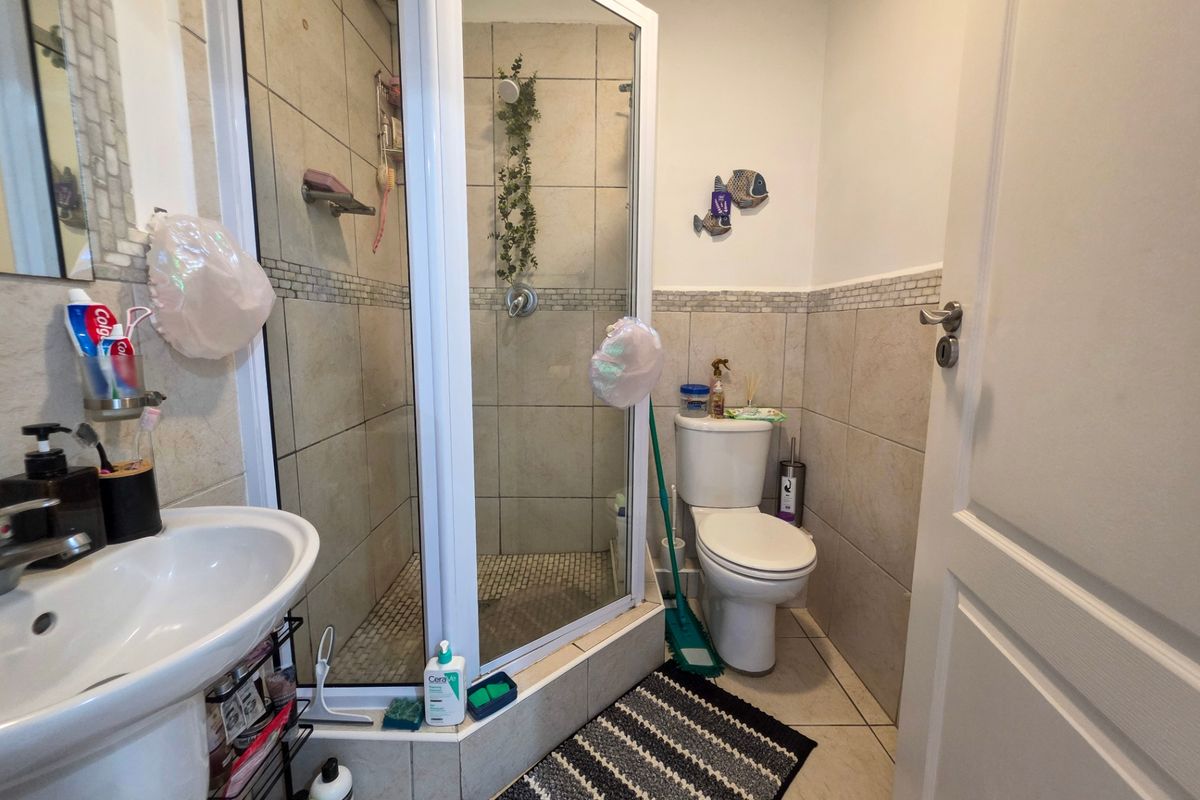 A functional bathroom featuring a corner shower enclosure, pedestal basin, and toilet with neutral ceramic wall and floor tiling.