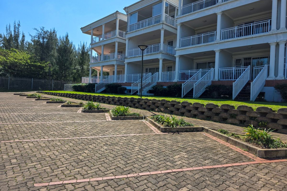 Rear view of a multi-story apartment complex featuring private balconies, paved parking bays, and landscaped retaining walls.