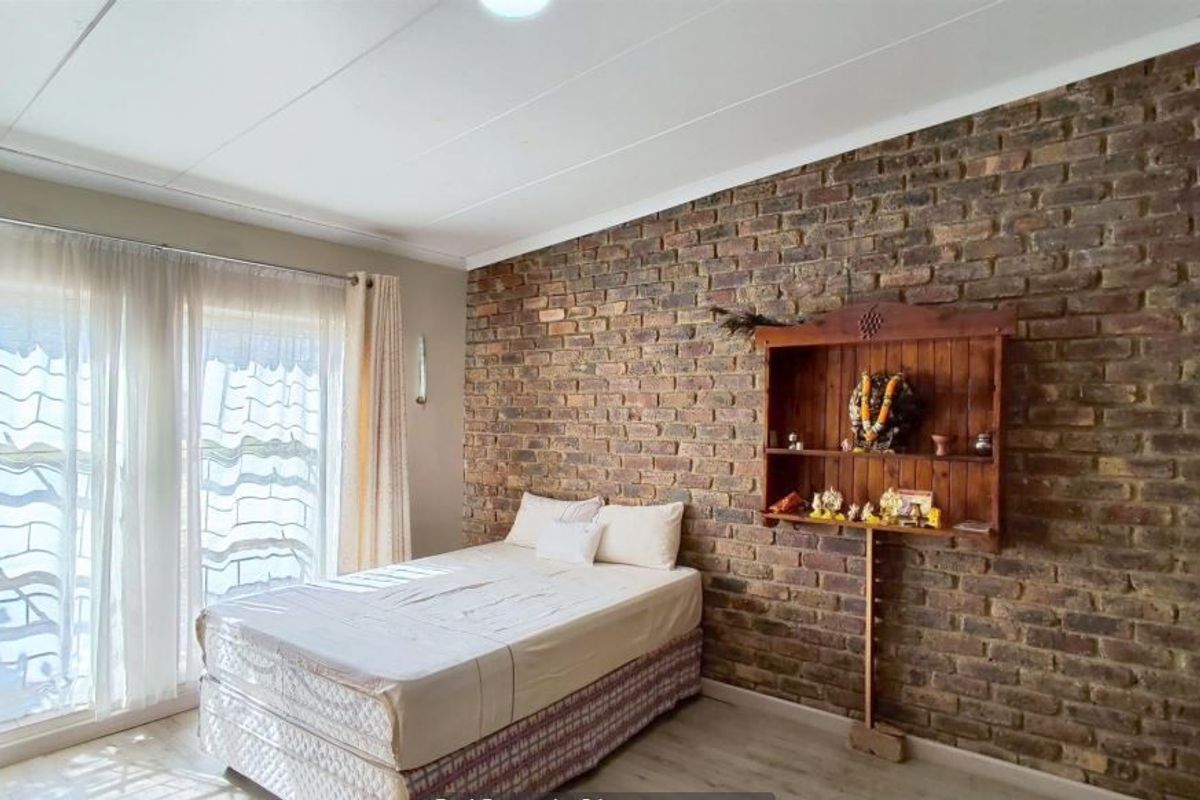 A bedroom featuring an exposed brick feature wall, laminate flooring, and a sliding glass door providing natural light.