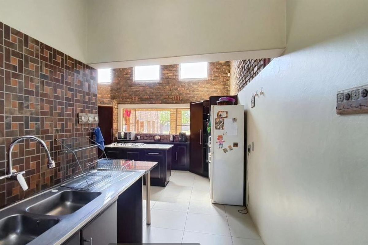 Kitchen featuring exposed brick walls, high ceilings, tiled flooring, and dark cabinetry with a double bowl stainless steel sink.
