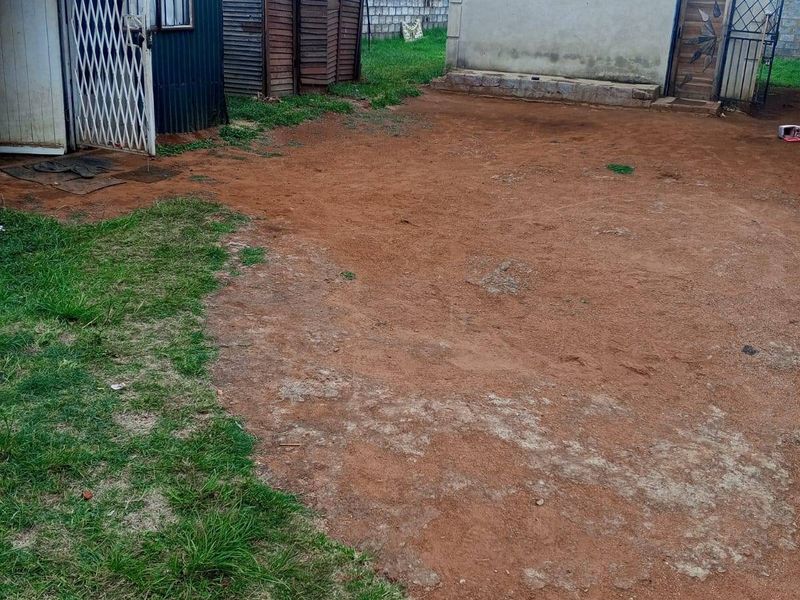 Rear yard area featuring multiple outbuildings with corrugated metal and masonry construction, set on an unpaved ground surface.