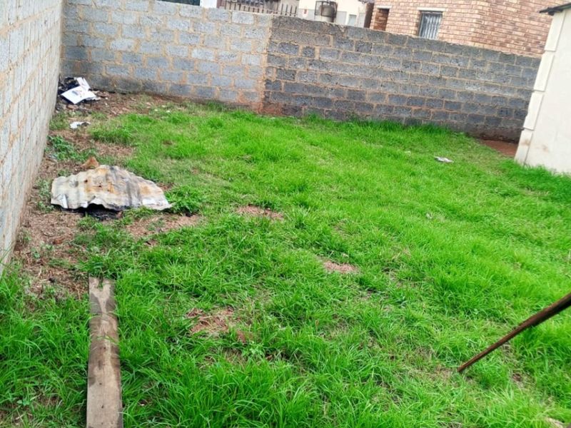 A rear yard area featuring a grass lawn enclosed by unfinished concrete block boundary walls.