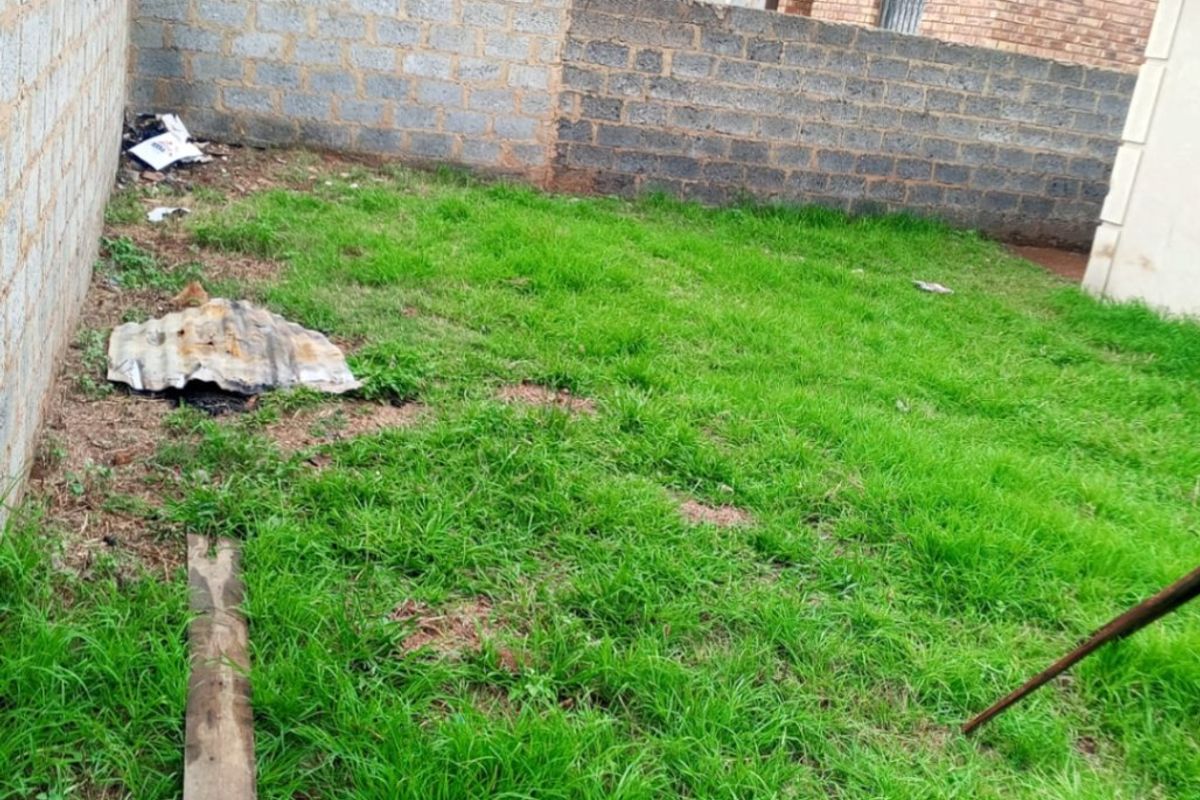 A rear yard area featuring a grass lawn enclosed by unfinished concrete block boundary walls.