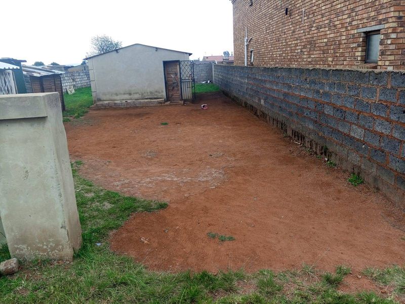 A spacious rear yard featuring a brick boundary wall and a detached outbuilding, offering significant potential for landscaping and outdoor improvement.