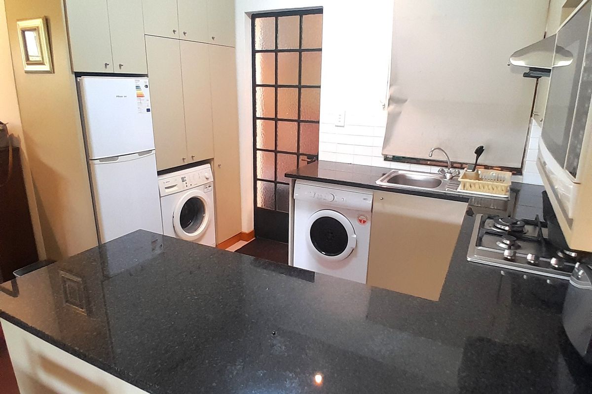 Compact kitchen featuring granite countertops, built-in cabinetry, gas hob, extractor fan, and integrated laundry space with direct access to an exterior door.