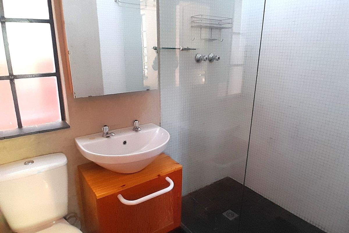 A compact bathroom featuring a vessel sink on a wooden vanity, a glass-enclosed shower, and a ceramic toilet.