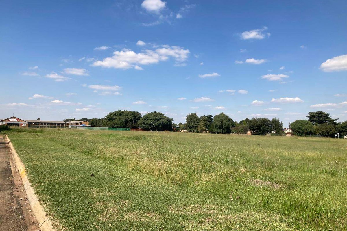 A view of a vacant residential plot featuring open grassland and a paved curb along the street frontage.