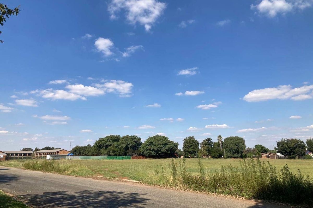 A view of the street frontage and adjacent vacant residential land, featuring established trees and a clear road access point.