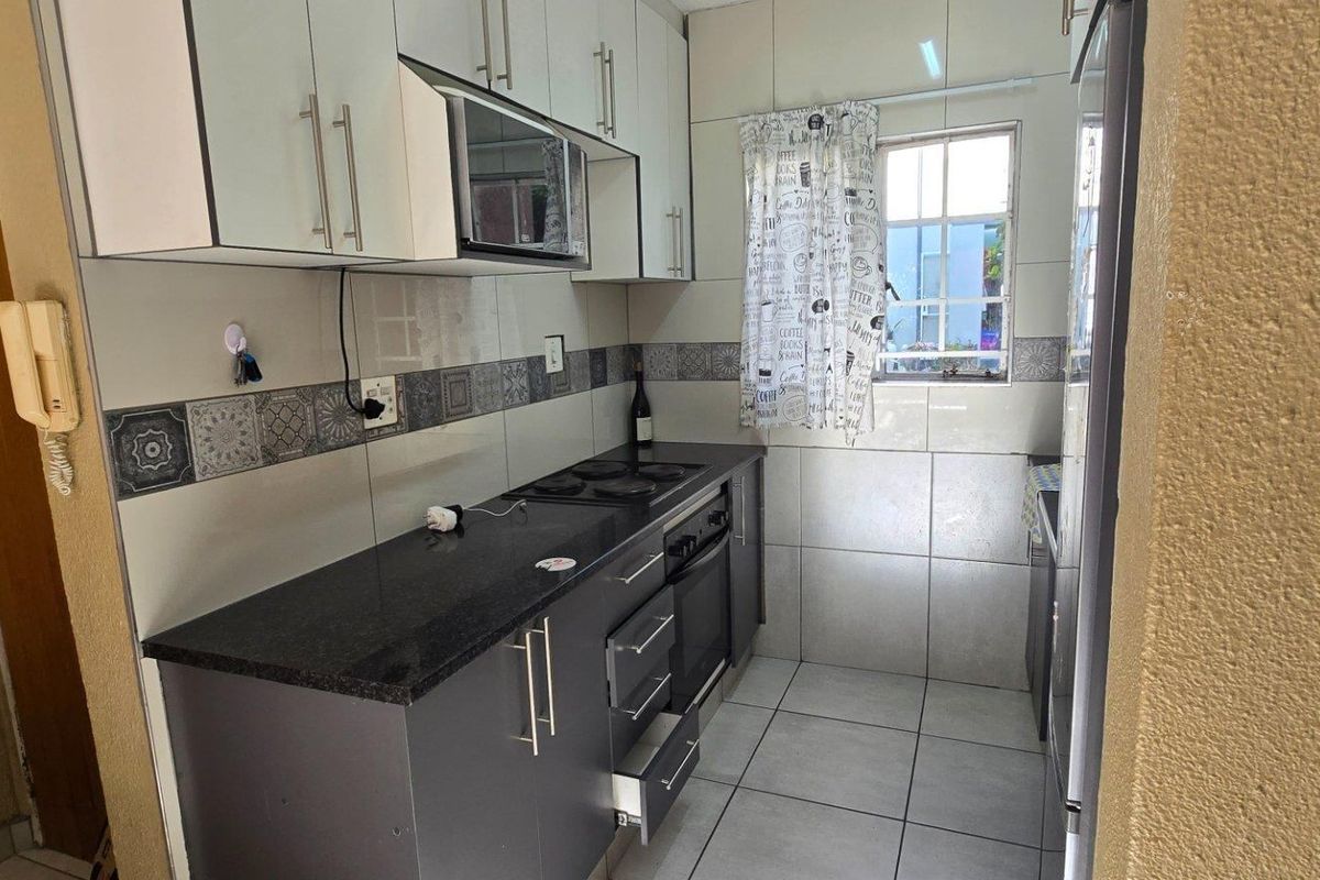 Compact kitchen featuring dark cabinetry, granite countertops, built-in oven and hob, and tiled finishes throughout.