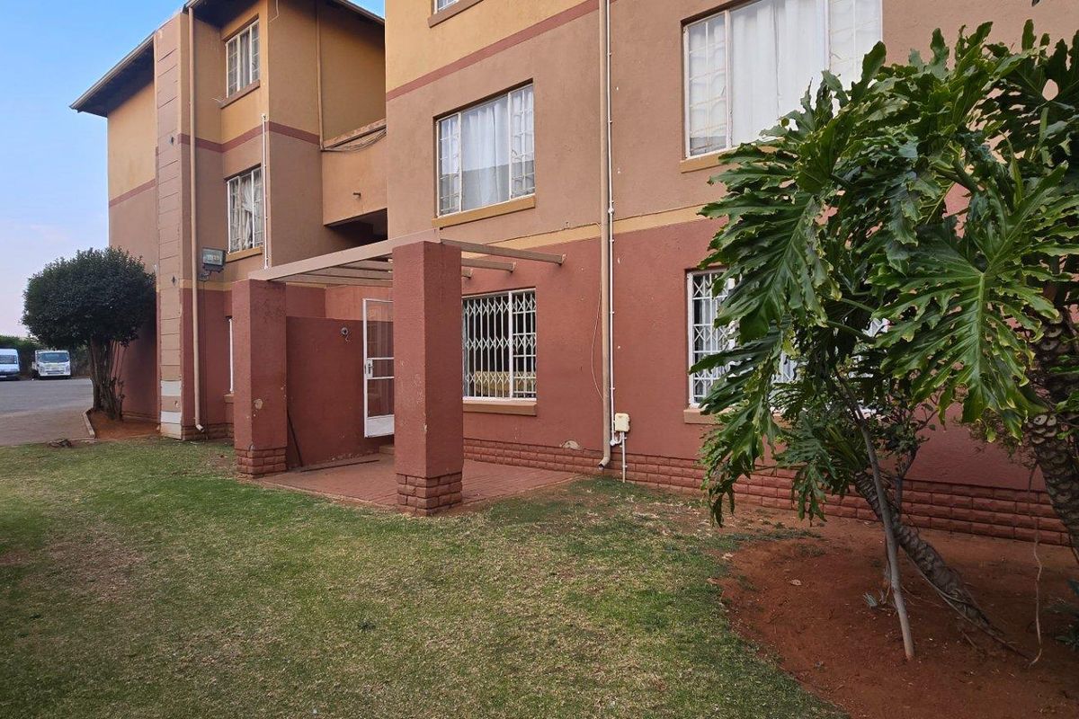 Rear view of the apartment building featuring a small covered patio area, security bars on windows, and a shared garden space.