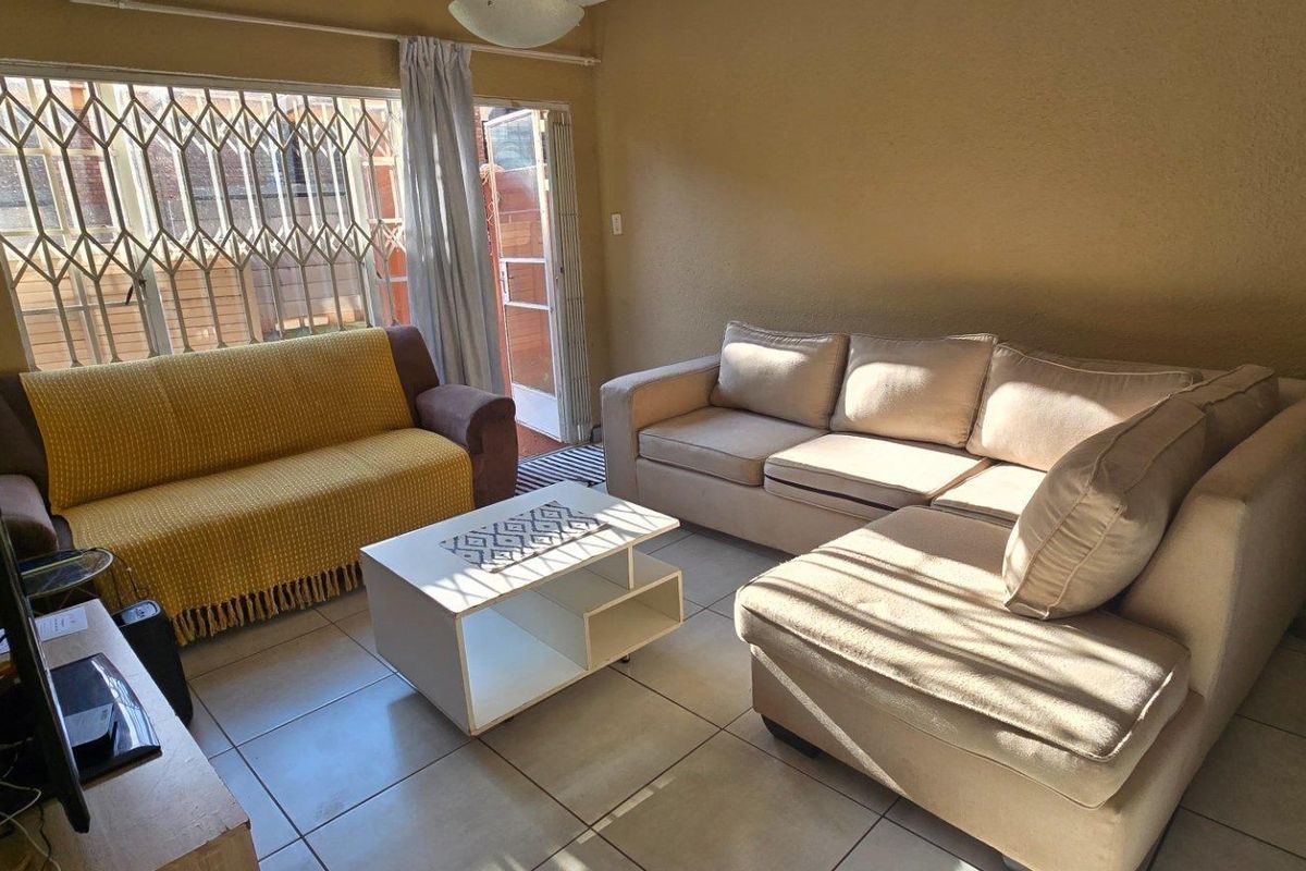 A living room featuring tiled flooring and a security gate leading to an outdoor area, providing natural light and access to the exterior.