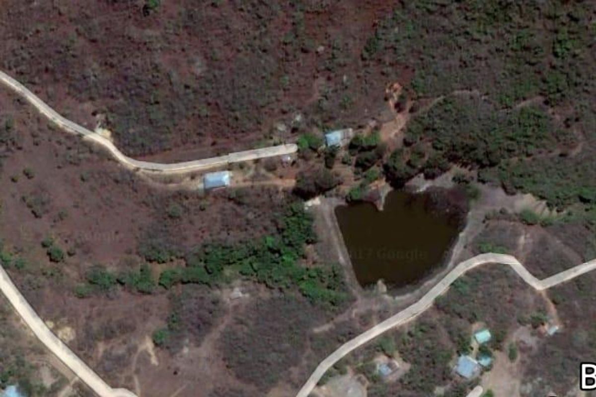 Aerial satellite view of the farm property showing access roads, natural landscape, and a small dam on the site.
