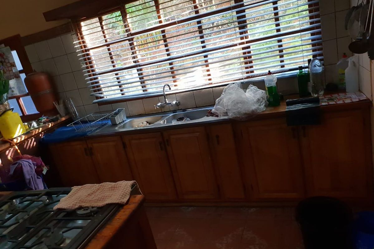 A functional kitchen featuring wooden cabinetry, a double basin sink, tiled backsplash, and a built-in gas hob with natural light from the window.