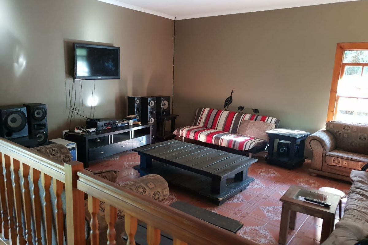 A living room featuring tiled flooring, a wooden balustrade, and a wooden window frame, with visible wall-mounted television and exposed wiring.
