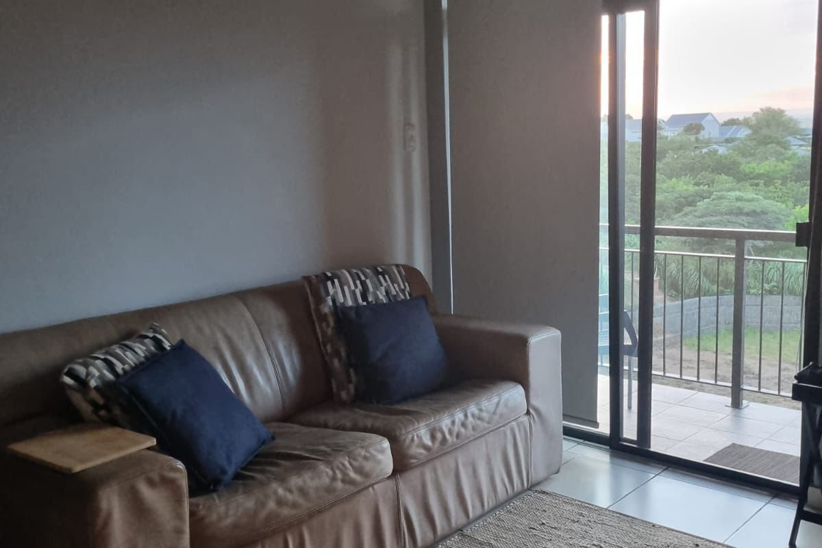 A living room area featuring tiled flooring and a large sliding glass door that provides access to an outdoor balcony.