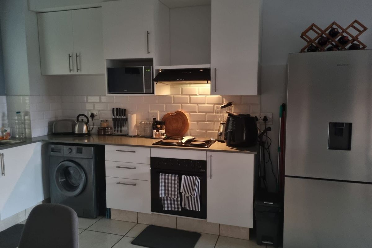 A functional kitchen featuring white cabinetry, subway tile backsplash, integrated appliances including an oven, hob, extractor fan, and built-in microwave with tiled flooring.