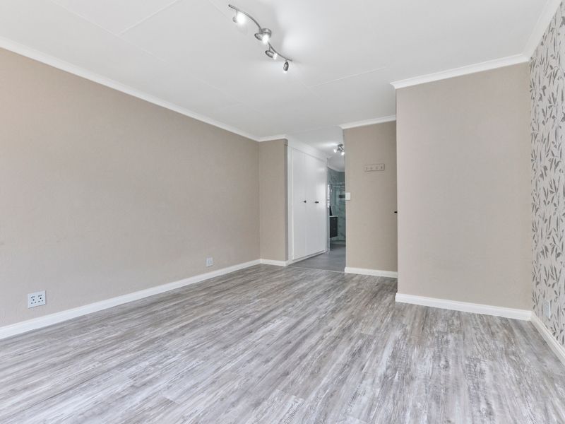A bright, empty living room featuring modern laminate flooring, neutral wall tones, a decorative feature wall, and built-in storage cupboards.