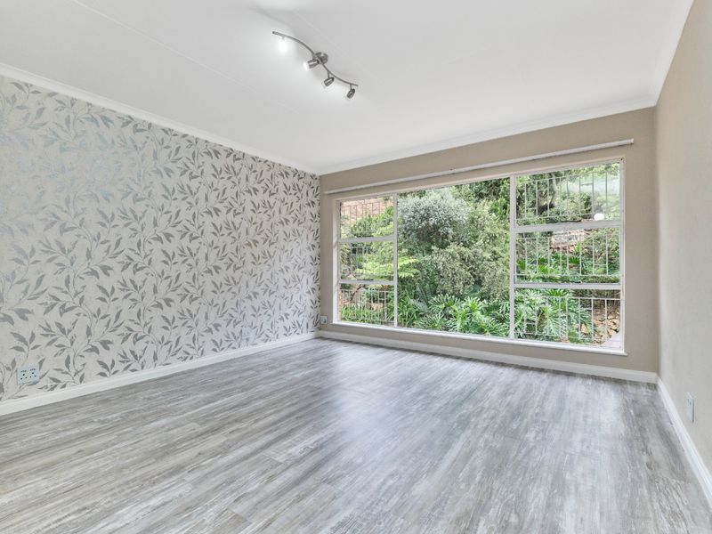 Bright and spacious living area featuring modern laminate flooring, a decorative feature wall, and a large window overlooking a lush garden.