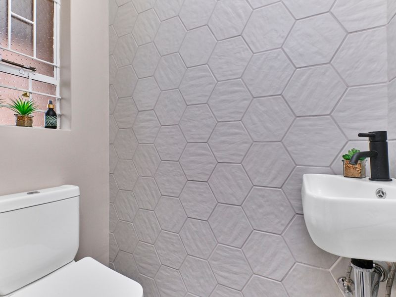 Modern guest bathroom featuring contemporary hexagonal wall tiling, a sleek wall-mounted basin with matte black fixtures, and a clean, minimalist aesthetic.