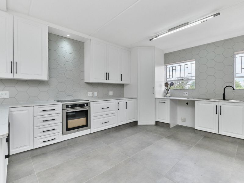 Modern kitchen featuring white cabinetry, stone countertops, hexagonal tile backsplash, built-in oven, and hob, with large format floor tiles.