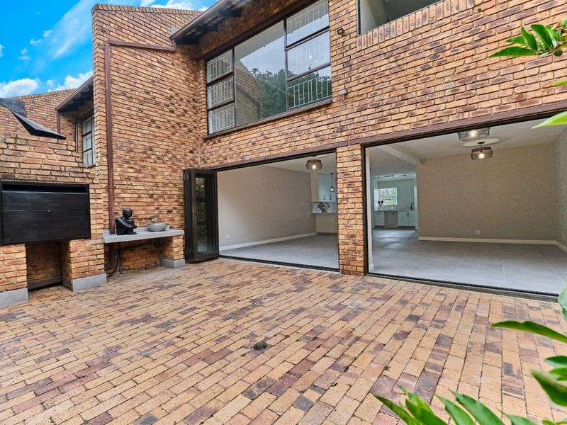Rear patio area featuring brick paving, a built-in braai, and large folding doors providing seamless access to the interior living space.