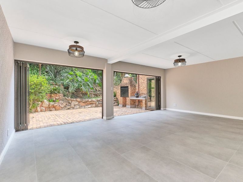 Spacious open-plan living area featuring large stacking doors that open onto a private patio with a built-in brick braai and garden views.