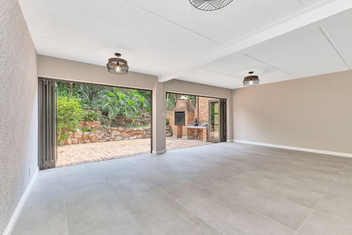 Spacious open-plan living area featuring large stacking doors that open onto a private patio with a built-in brick braai and garden views.