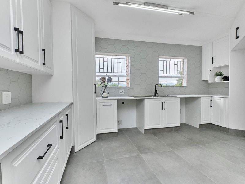 A modern, renovated kitchen featuring white shaker cabinetry, quartz countertops, a stylish hexagonal tile backsplash, and large format grey floor tiles.
