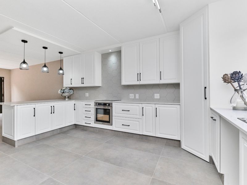 Modern, well-appointed kitchen featuring white shaker-style cabinetry, stone countertops, a stylish hexagonal tile backsplash, and integrated appliances with sleek black hardware.