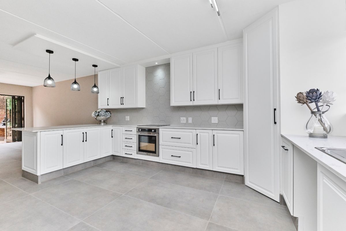 Modern, well-appointed kitchen featuring white shaker-style cabinetry, stone countertops, a stylish hexagonal tile backsplash, and integrated appliances with sleek black hardware.