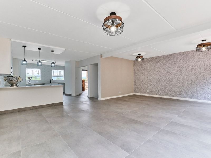 Spacious open-plan living and kitchen area featuring large format floor tiles, modern pendant lighting, and a functional kitchen island with built-in cabinetry.