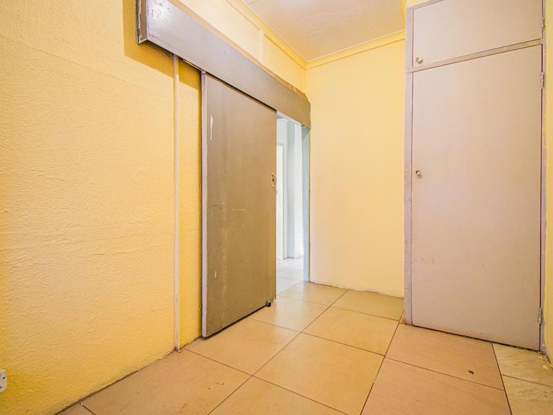 A functional hallway featuring tiled flooring, a sliding door, and a built-in storage cupboard, presenting a blank canvas for interior updates.