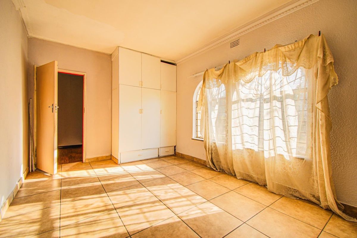 An empty bedroom featuring tiled flooring, built-in cupboards, and an arched window, offering a blank canvas for renovation.
