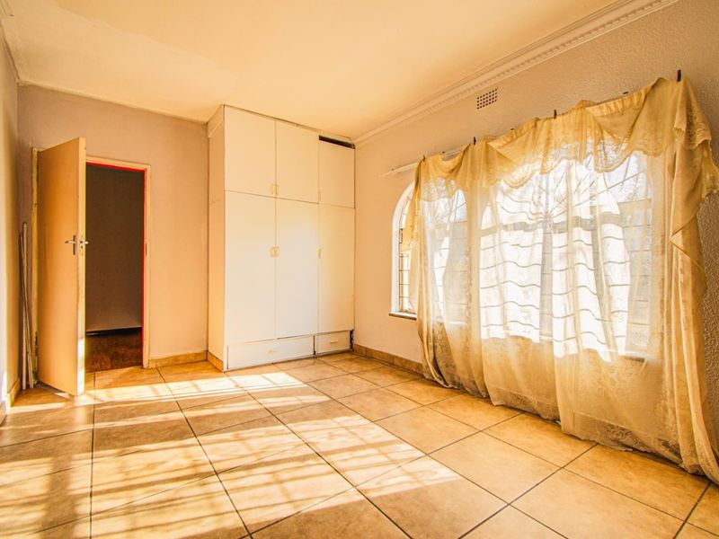 An empty bedroom featuring tiled flooring, built-in cupboards, and an arched window, offering a blank canvas for renovation.