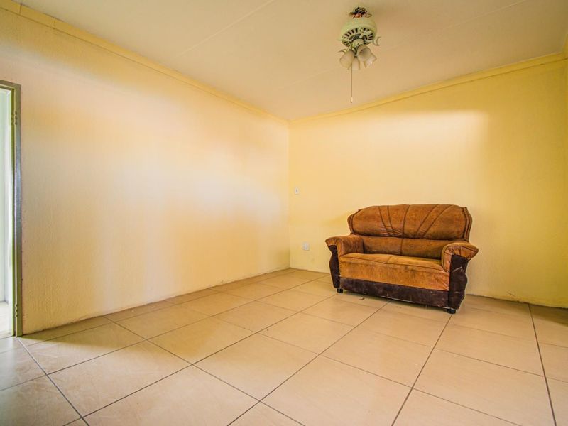 A simple living room featuring neutral tiled flooring and a ceiling fan, providing a blank canvas for potential interior design updates.