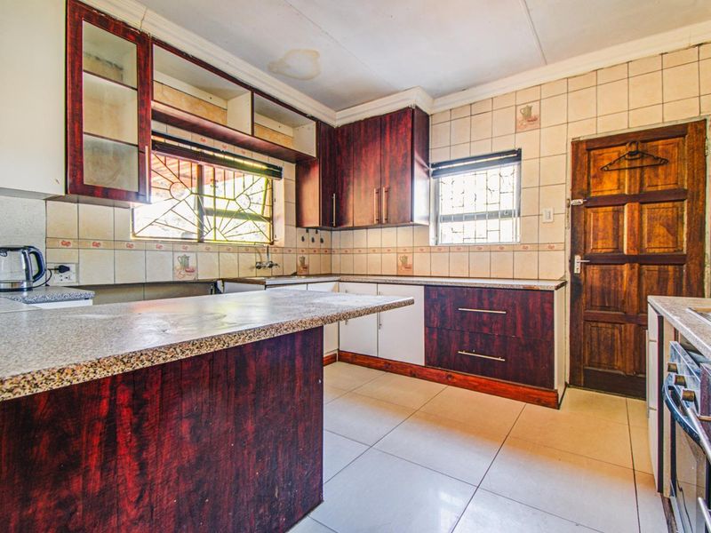A dated kitchen featuring laminate cabinetry, granite-look countertops, and ceramic tiling, requiring cosmetic updates to modernize the space.