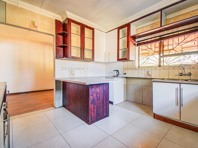 A dated kitchen featuring built-in cabinetry, tiled splashbacks, and tiled flooring, offering a functional layout ready for modernization.