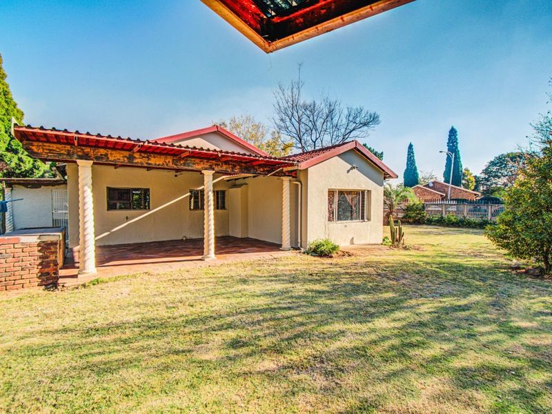 Rear view of the house featuring a covered patio with decorative columns, a built-in brick braai, and a spacious garden area.