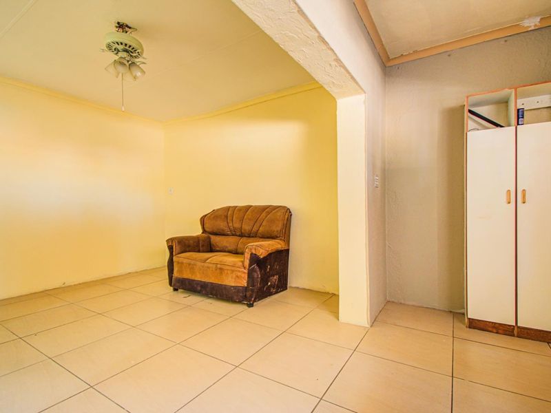 A living area featuring tiled flooring, a ceiling fan, and a built-in cupboard, requiring cosmetic updates to improve its overall condition.