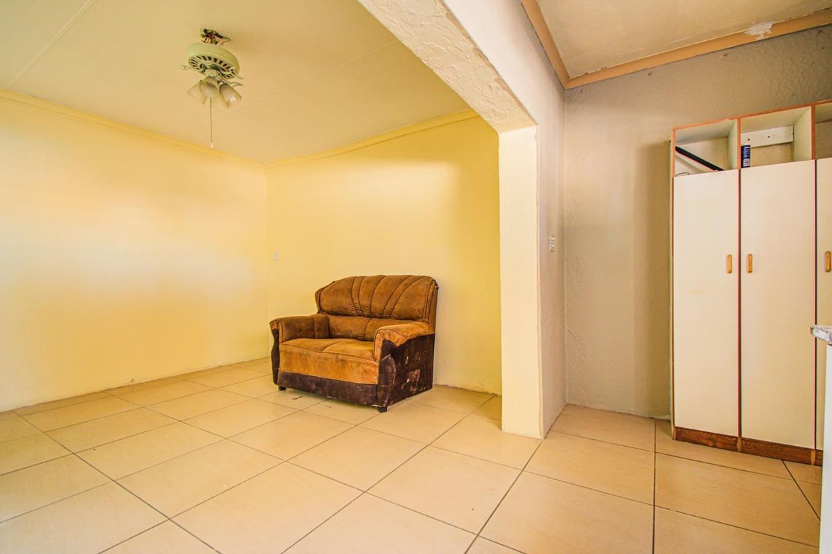 A living area featuring tiled flooring, a ceiling fan, and a built-in cupboard, requiring cosmetic updates to improve its overall condition.