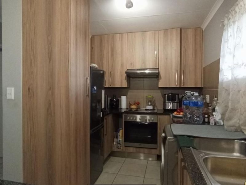 A functional kitchen featuring wood-look cabinetry, stainless steel sink, built-in oven with extractor fan, and tiled flooring.