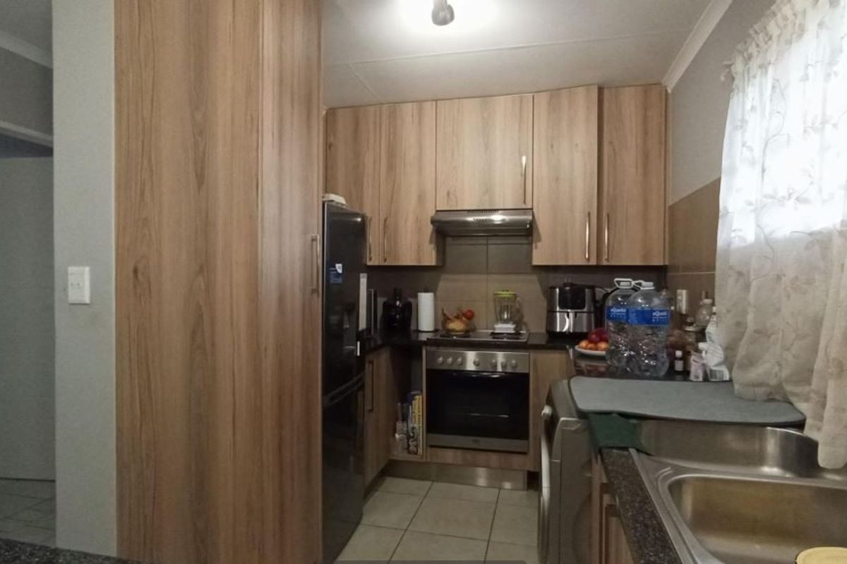 A functional kitchen featuring wood-look cabinetry, stainless steel sink, built-in oven with extractor fan, and tiled flooring.