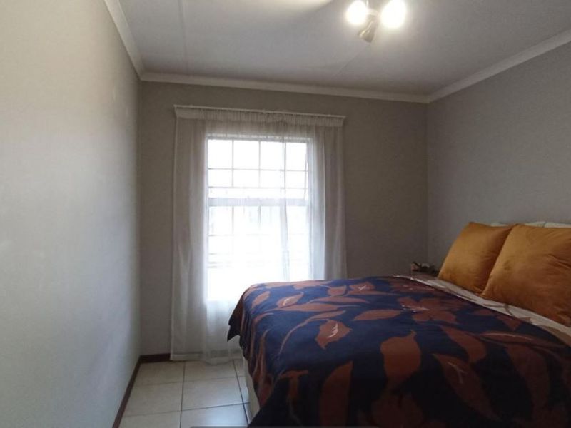 A simple bedroom featuring tiled flooring, neutral wall paint, and a window with a curtain track.