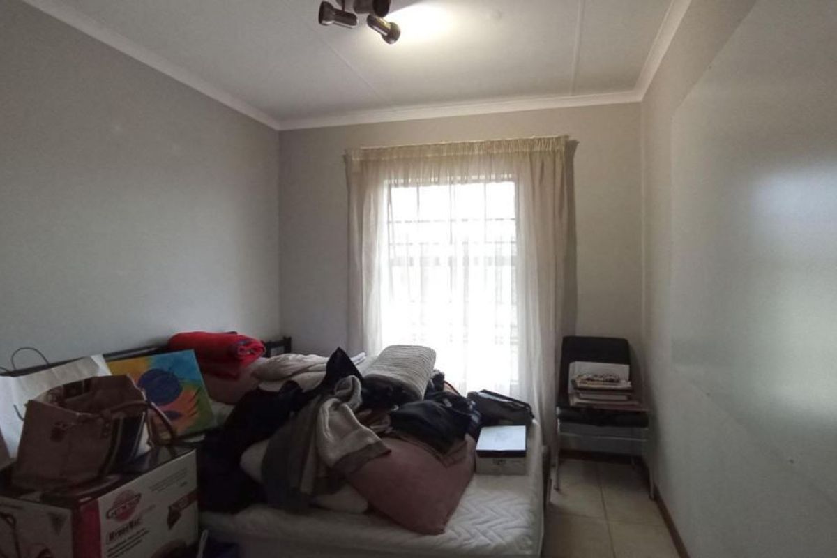 A bedroom featuring tiled flooring, a ceiling light fixture, and a window fitted with security bars.