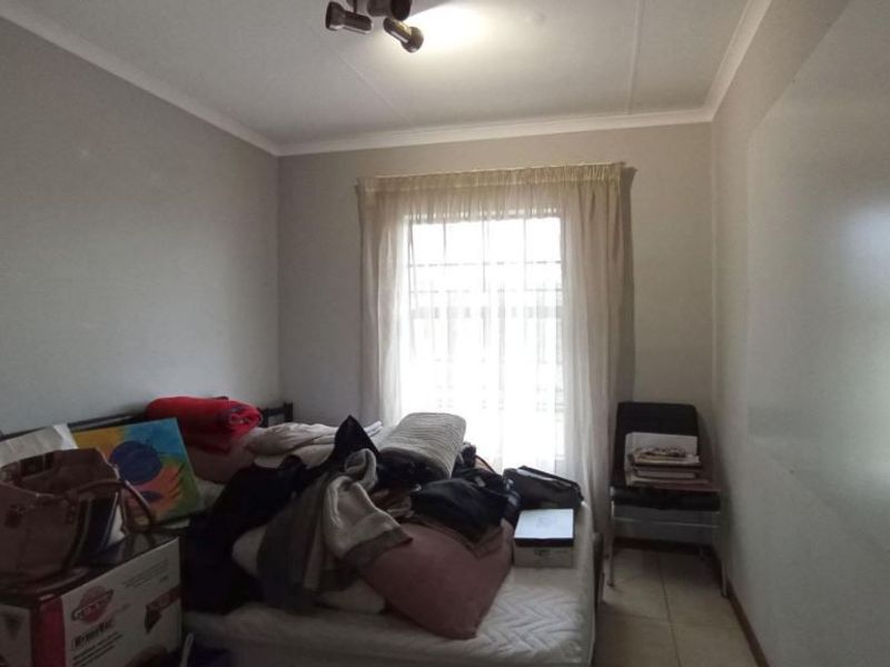A bedroom featuring tiled flooring, a ceiling light fixture, and a window fitted with security bars.