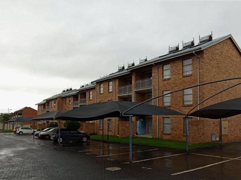 Exterior view of a multi-story face brick apartment complex featuring covered parking bays and rooftop solar water heating systems.