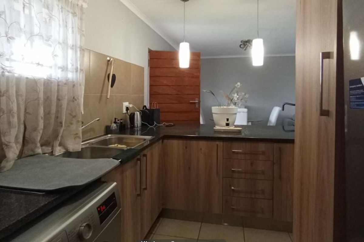 A functional kitchen featuring laminate cabinetry, granite countertops, a double basin sink, and a breakfast bar, seamlessly connecting to the adjacent living area.