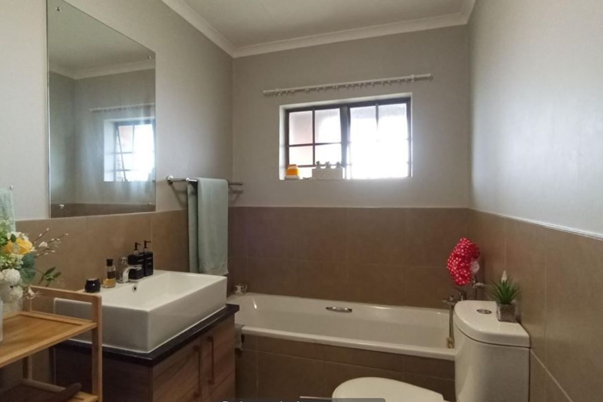 A well-maintained bathroom featuring a modern vessel sink on a vanity cabinet, a bathtub, and neutral wall tiling.